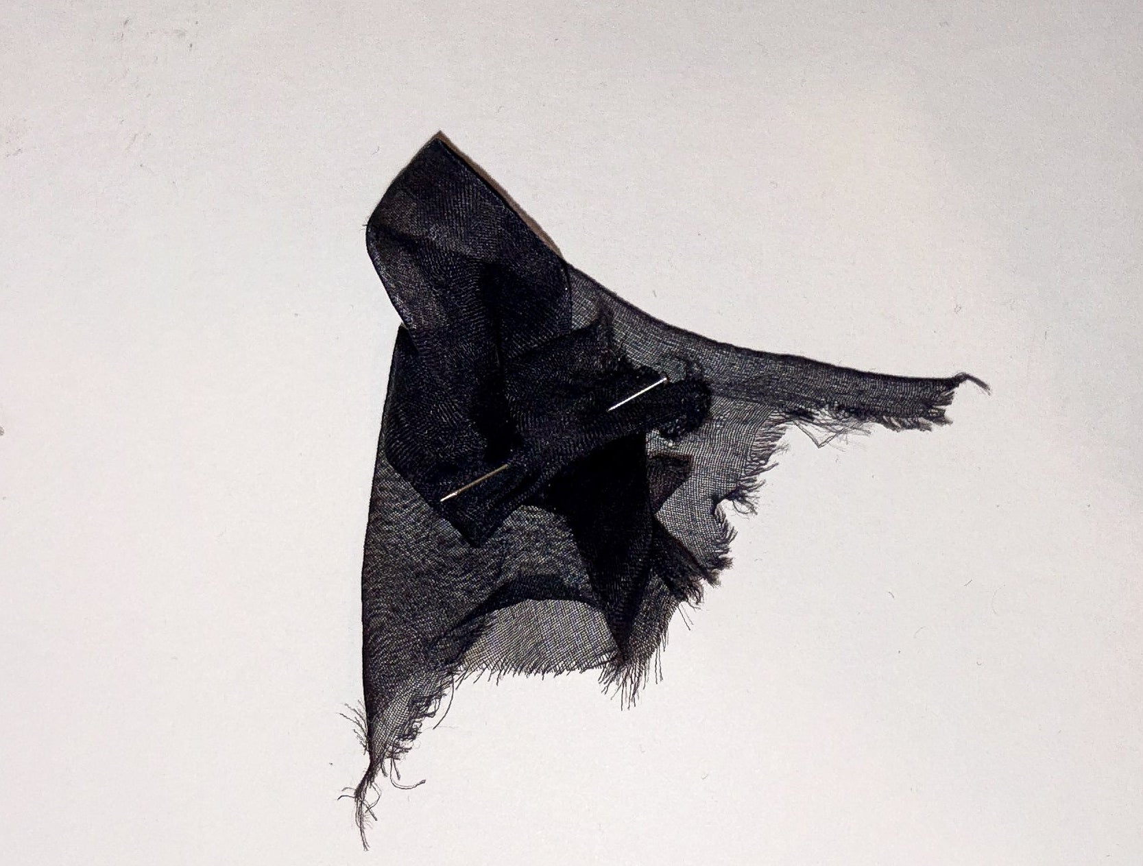 A black fabric sample swatch with raw, frayed edges, pinned to a white page of a ring-bound fabric book.